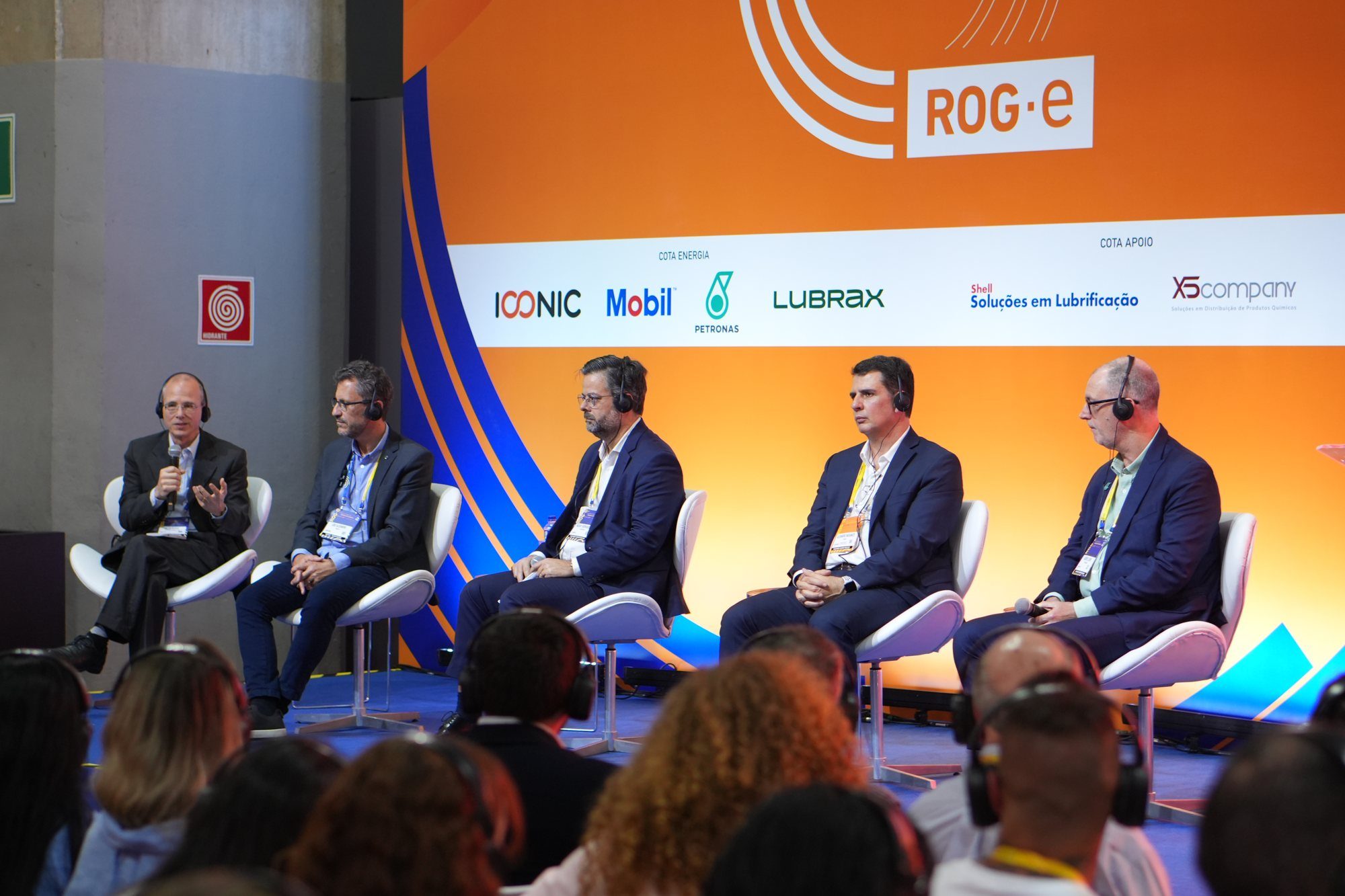 Painel com cinco palestrantes no palco da Arena