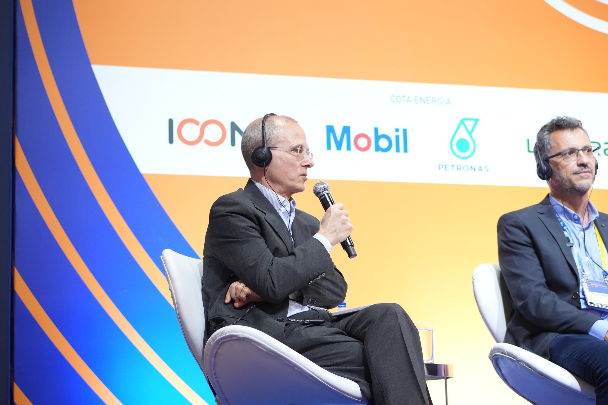 Palestrante falando ao microfone, com o logo Mobil ao fundo